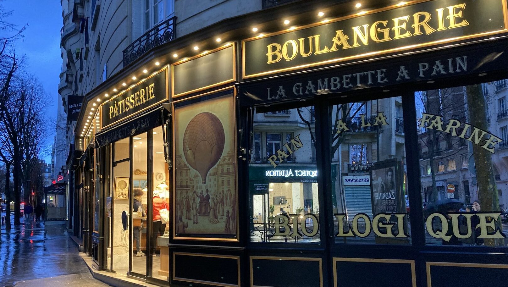 The lit-up facade of La Gambette à Pain bakery in Paris at dusk.