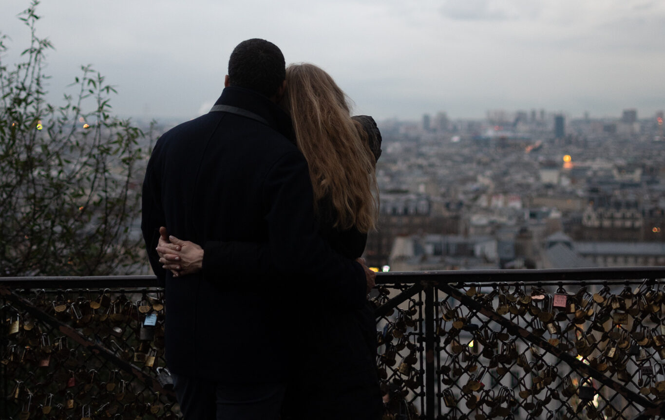 A couple holds each other tightly in front of a love lock clad gate in Montmartre.